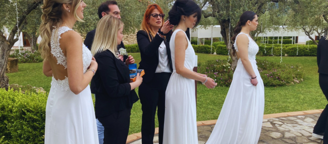 Tre modelle vestite da spose vengono sistemate dalle parrucchiere per uno shooting fotografico.