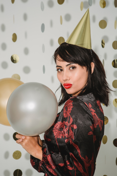 Ragazza con trucco impeccabile, cappello di festa a punta e pallone bianco celebrando il suo compleanno.